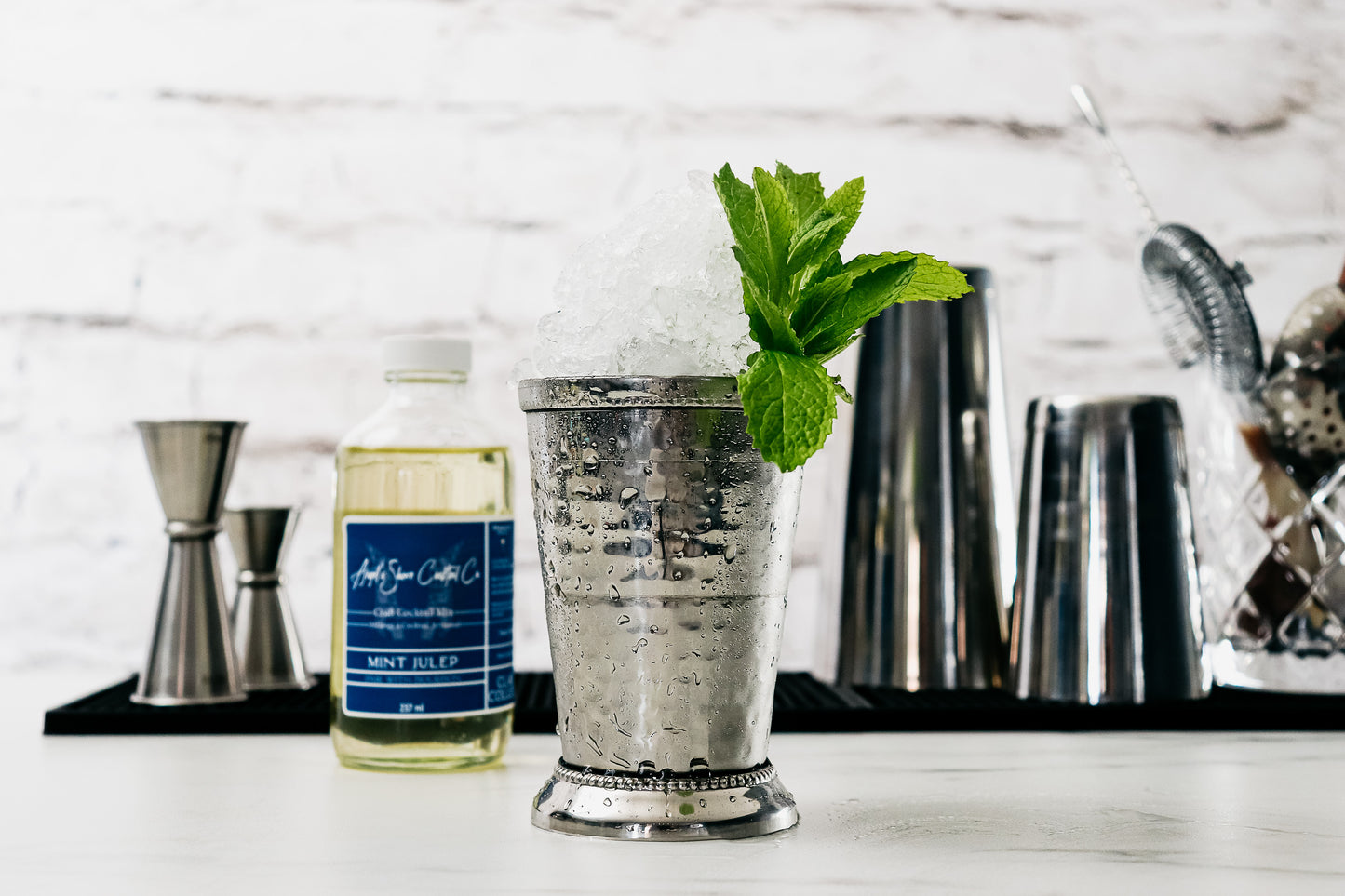 
                  
                    Mint Julep Cocktail in a julep tin cup, crushed ice, fresh mint bouquet, Craft Cocktail Mix bottle, presented on a bar with bar tools in the background . Angel's Share Cocktail Co. Winnipeg
                  
                